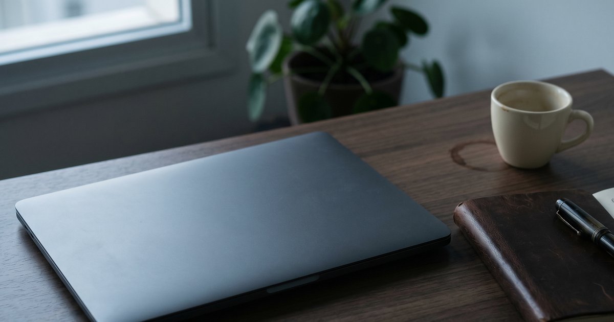 Notebook fechado em mesa de escritório com caderno e xícara de café