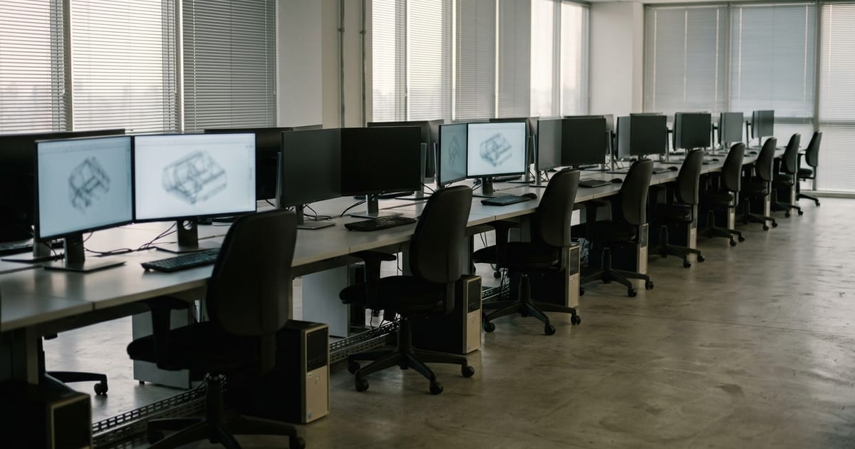 Escritório com estações de trabalho e monitores com desenhos técnicos, ilustrando o licenciamento de software proprietário